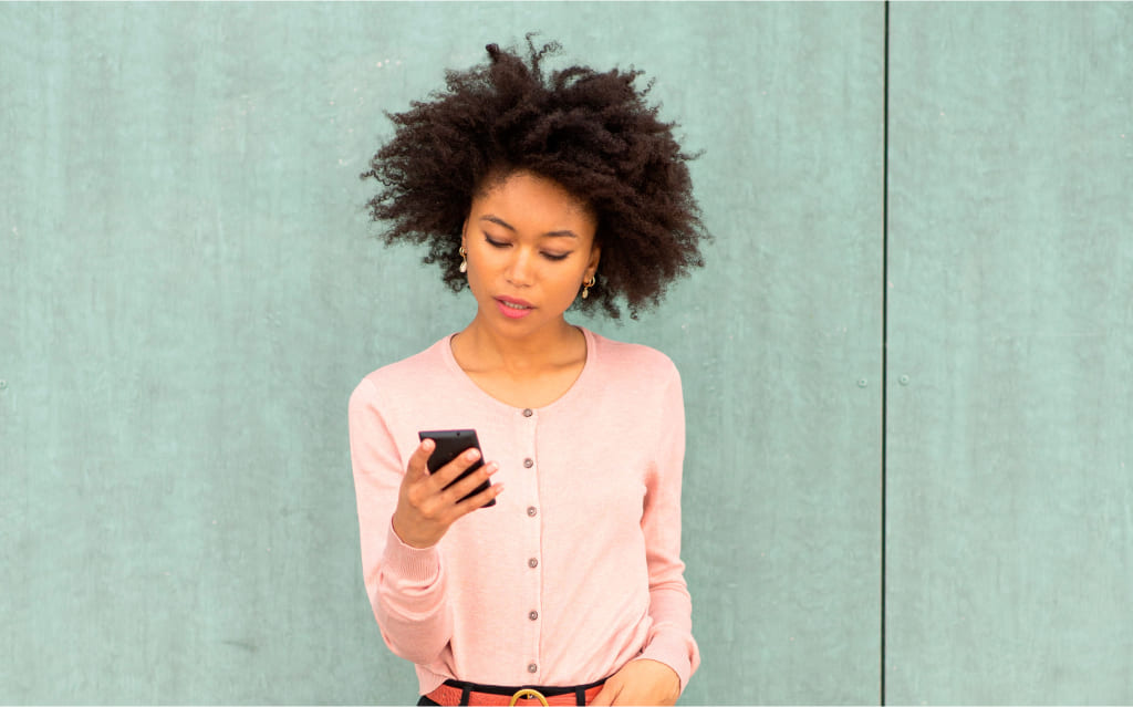 mulher negra em pé diante de parede segurando celular e pesquisando sobre os tipos de liquidez