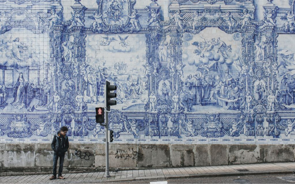 _viajar para Portugal  painel com típica azulejaria portuguesa com uma pessoa parada ao lado de um semáforo