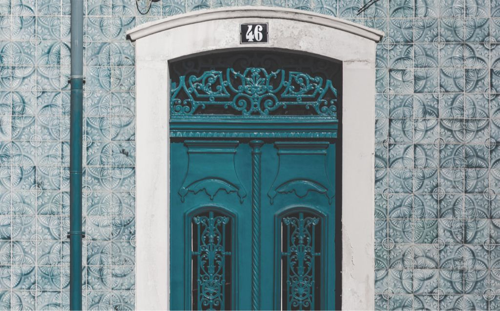  viajar para Portugal | porta grande feita em madeira na cor azul, número 46 acima da porta, a parede é feita de azulejos azuis