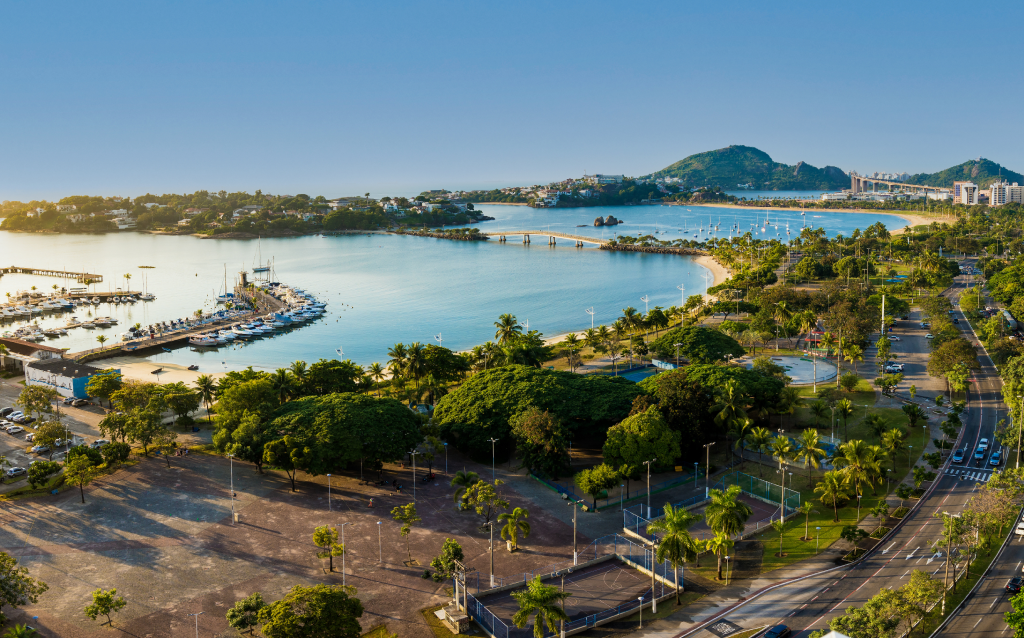 Vista panorâmica da praia com mar calmo, palm trees e área verde, ideal para relaxar e aproveitar o sol em um dia ensolarado.