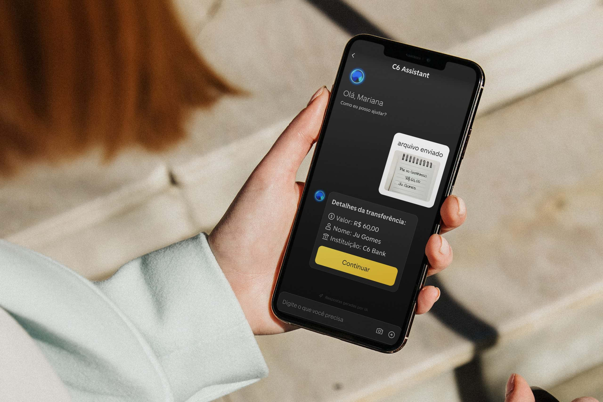 Uma pessoa segura um celular exibindo uma interface do "C6 Assistant". Na tela do celular, aparece a mensagem "Olá, Mariana, como posso ajudar?" e informações relacionadas a uma transferência, incluindo o valor de R$ 5.000, o nome do destinatário (Ju Gomes) e a instituição financeira (C6 Bank). Há também um botão amarelo com o texto "Continuar" e um campo para digitar. O fundo da imagem parece ser um ambiente interno com piso claro.