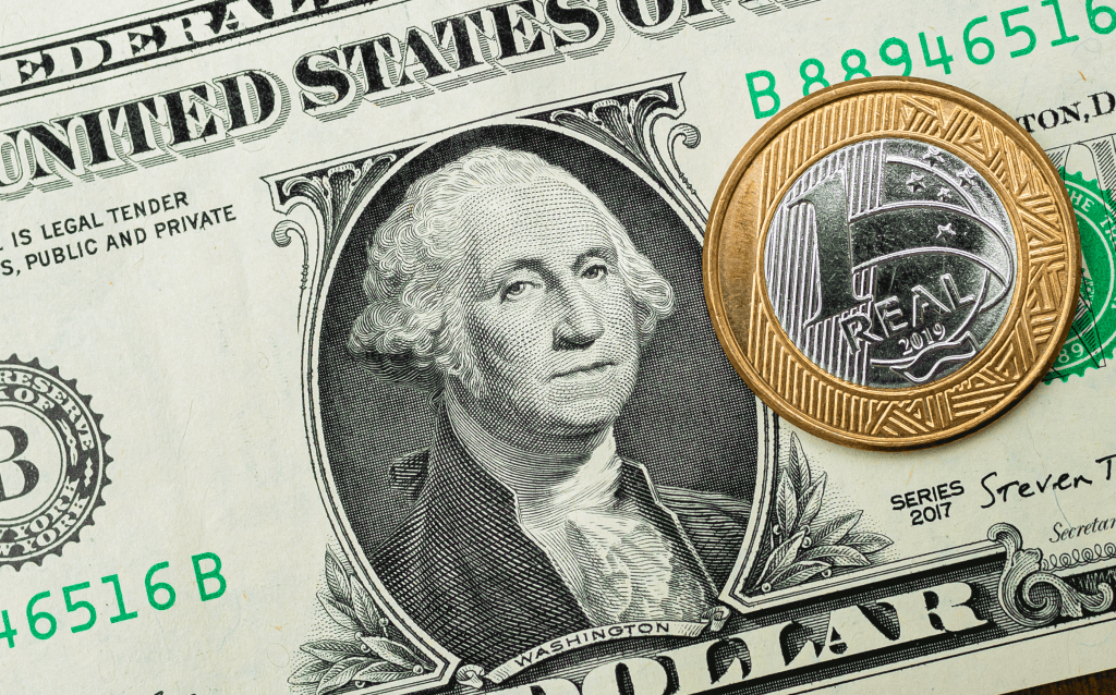 Nota de dólar com o rosto de Washington e uma moeda de um 1 real em cima
